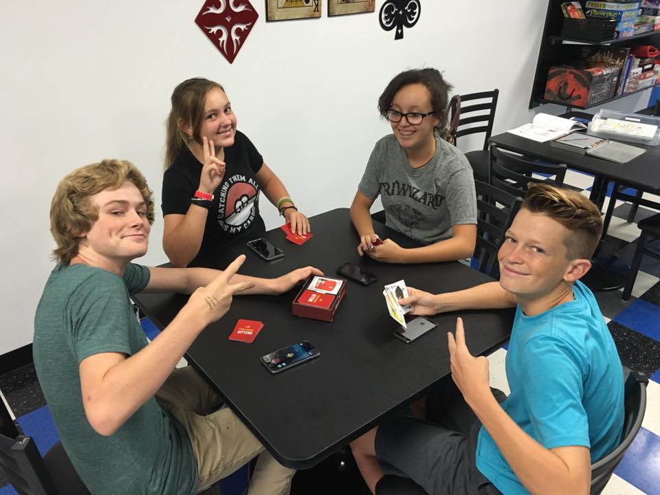 4 young adults playing the card game, Exploding Kittens, at Zanders Game House.