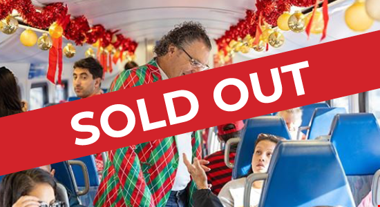 Metrolink CEO Darren Kettle, wearing a Red and Green Plaid blazer, is standing in the aisle of the Metrolink Holiday Express Train talking to someone.