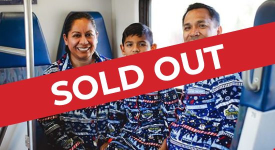 A mother, father, and young boy dressed in matching pajama sets smiling as they pose on the Metrolink Holiday Express Train.