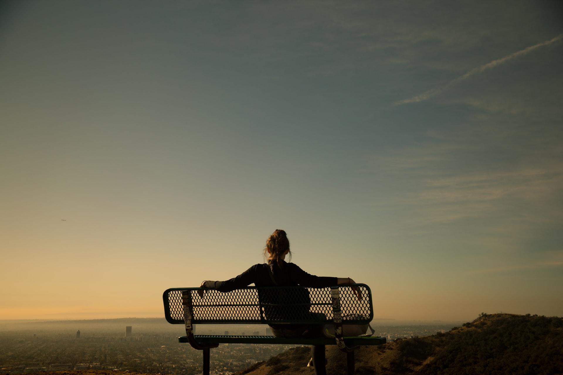 The back of a woman sitting on a park bench looking over Los Angeles 