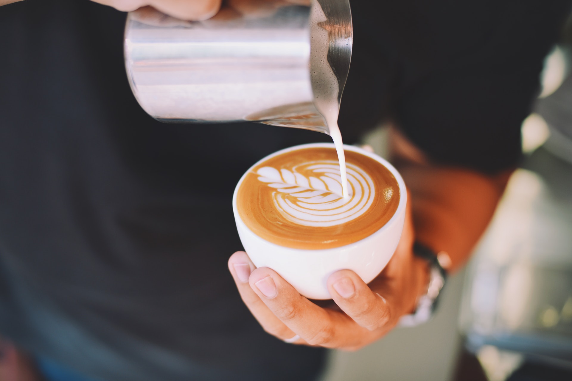 Steamed milk being poured into a latte to make a leaf design