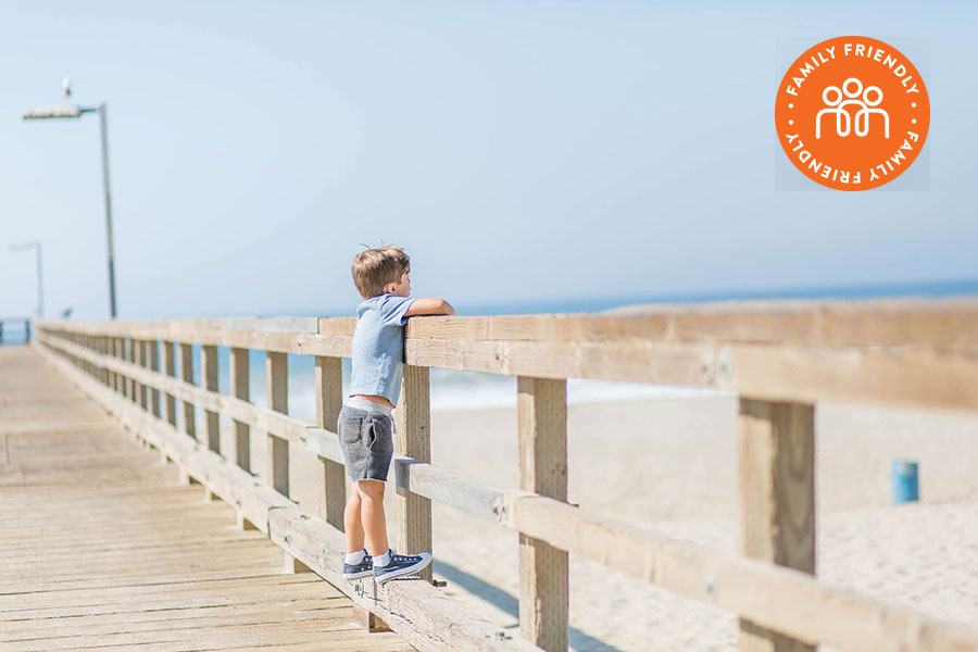 Young boy looking over the rail at Port Hueneme Pier. Image stamped with Family Friendly badge.